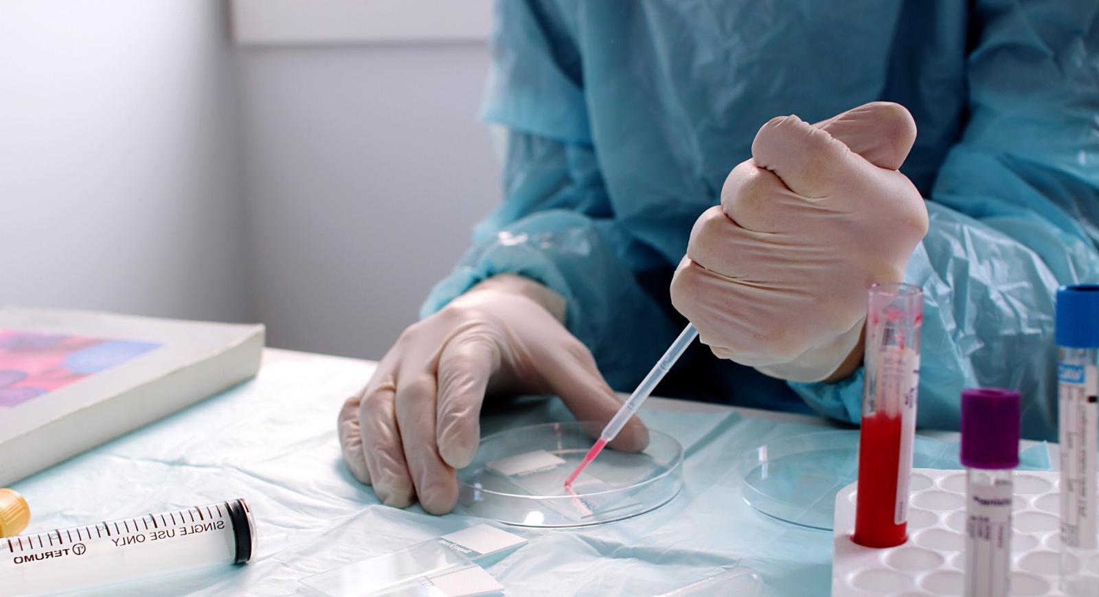 Photo of a scientist in protective lab gear transferring red liquid into a petri dish