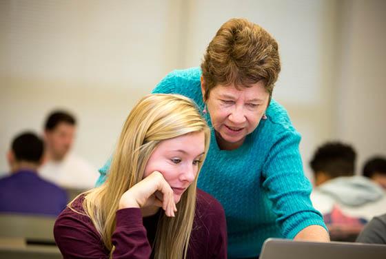 Photo of an older female 教师 member leaning over a Chatham University student 和 pointing to a computer