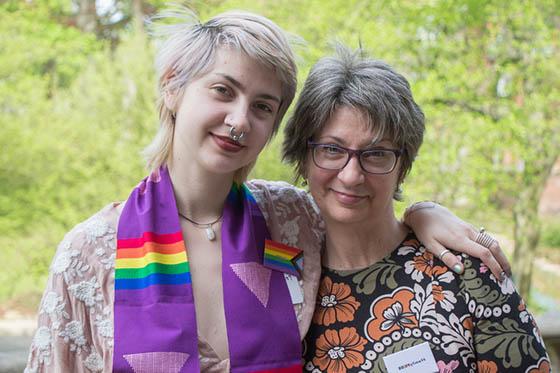 Photo of a graduating Chatham University student wearing a rainbow stole, with an arm over the shoulder of a parent or guardian